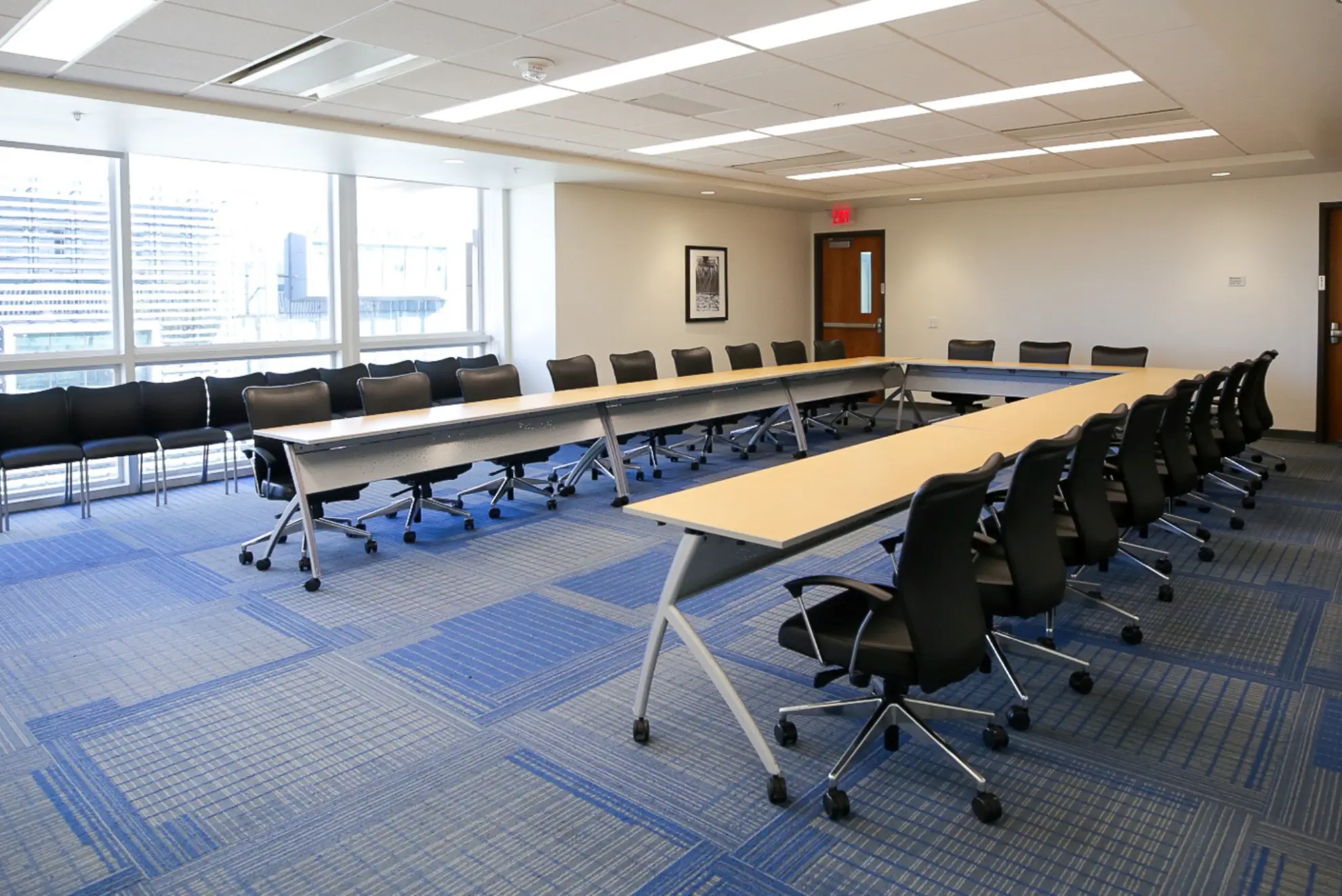 A conference room with a long table and chairs, featuring windows and a door.
